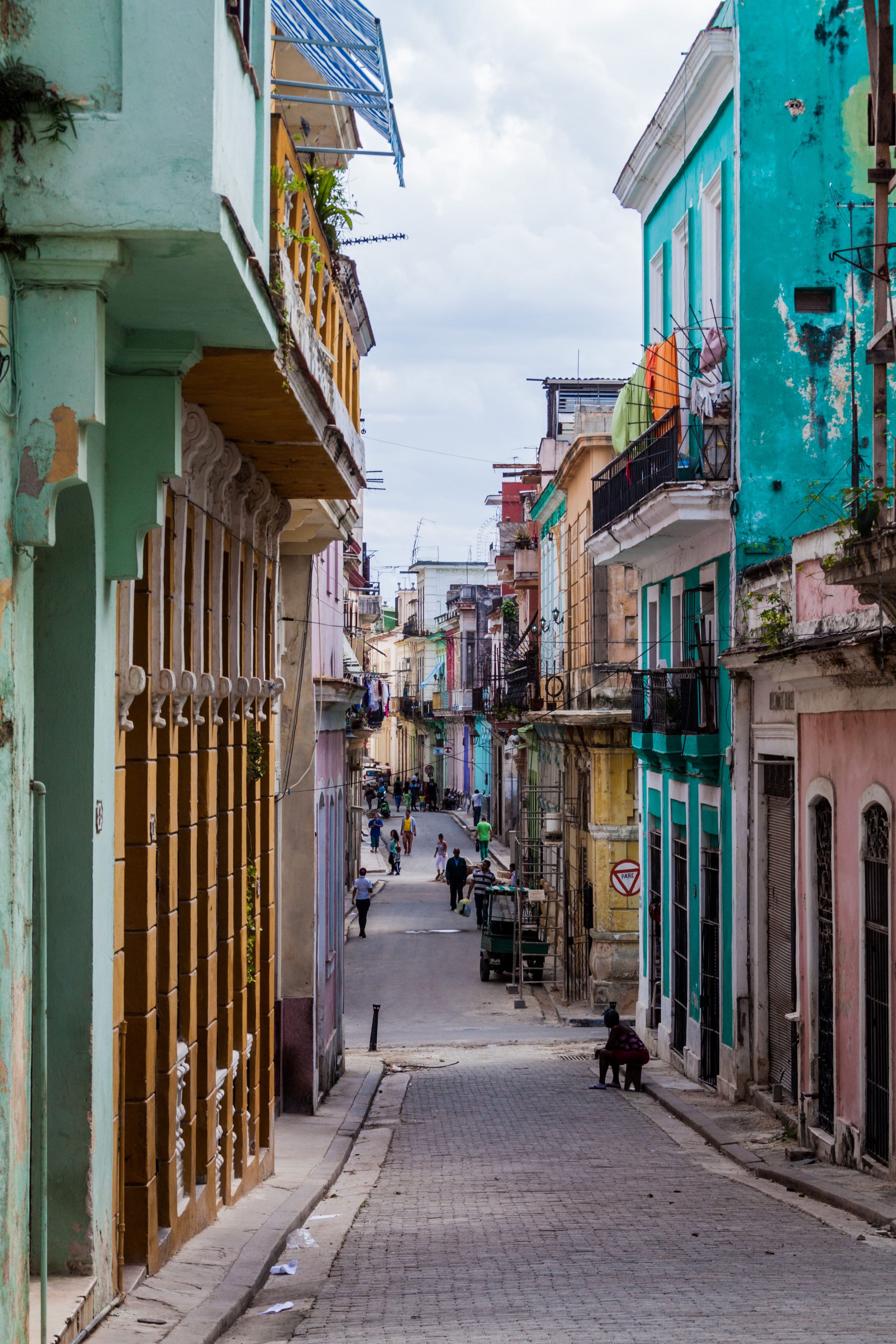Narrow Havana street with turquoise and pastel colonial buildings, balconies, and pedestrians, Cuba