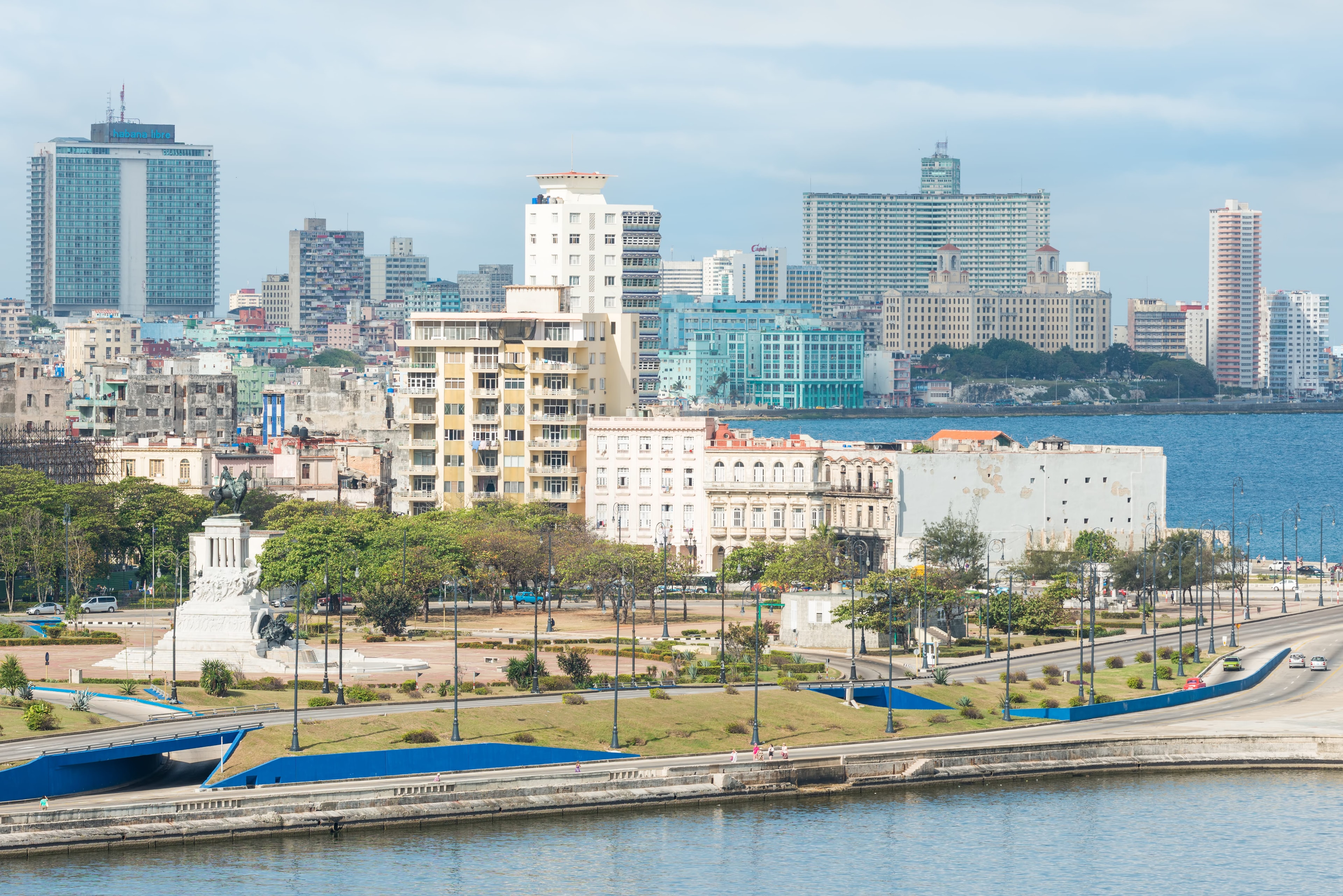 Havana Malecón waterfront with monument, tree-lined promenade, and modern skyline across the bay, Cuba