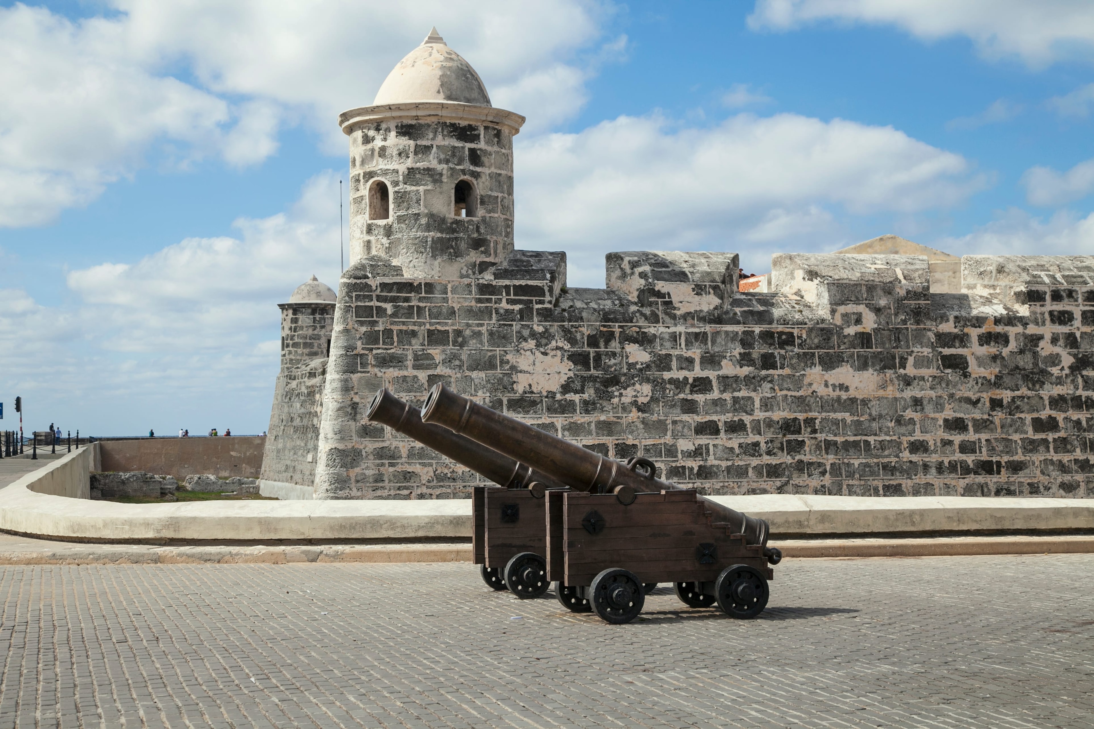 Bronze cannon on wooden carriage in front of stone fortress tower, Havana Cuba