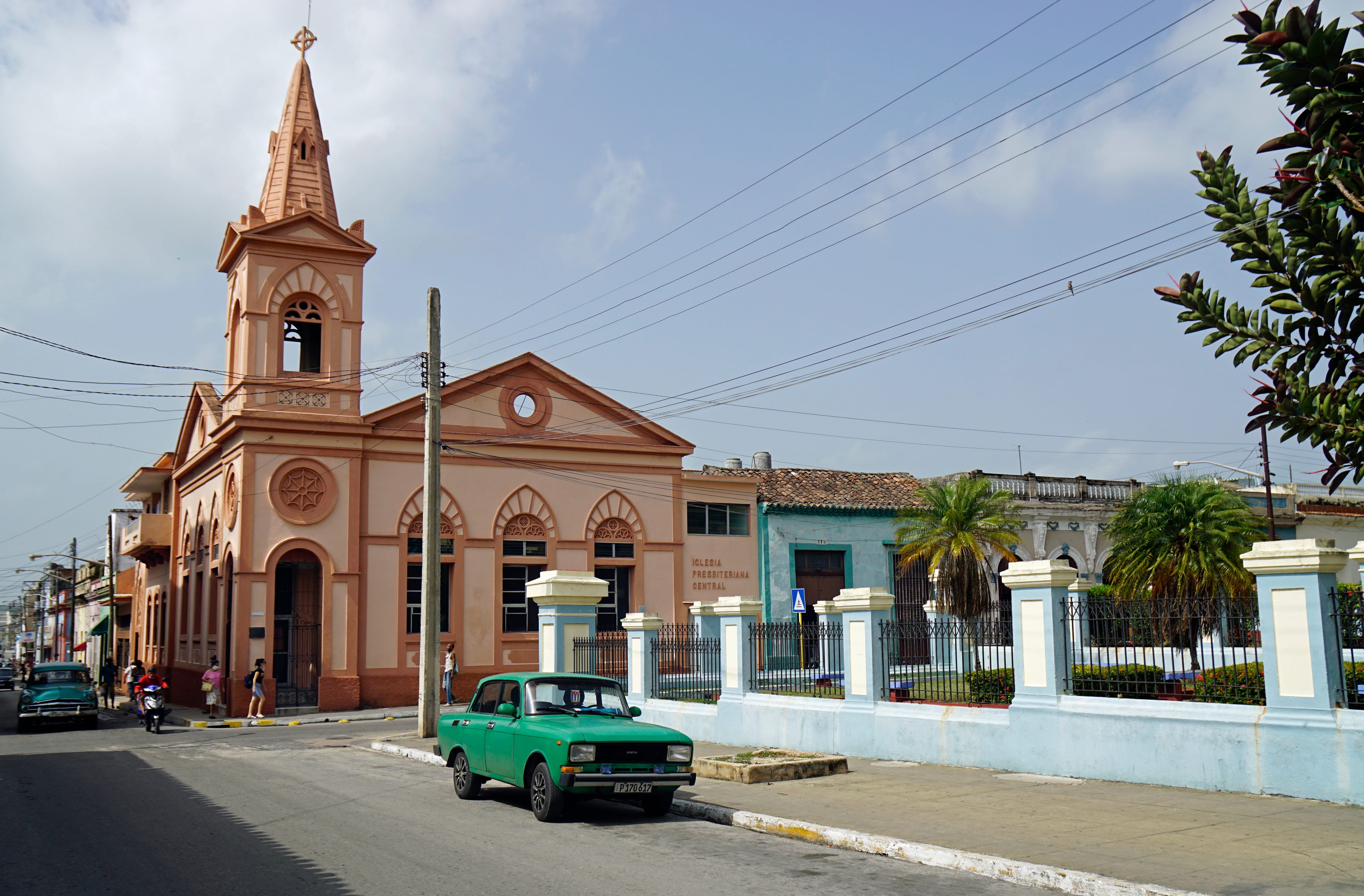 Iglesia Presbiteriana Central salmon-pink church with pointed bell tower and green vintage car on street, Cuba