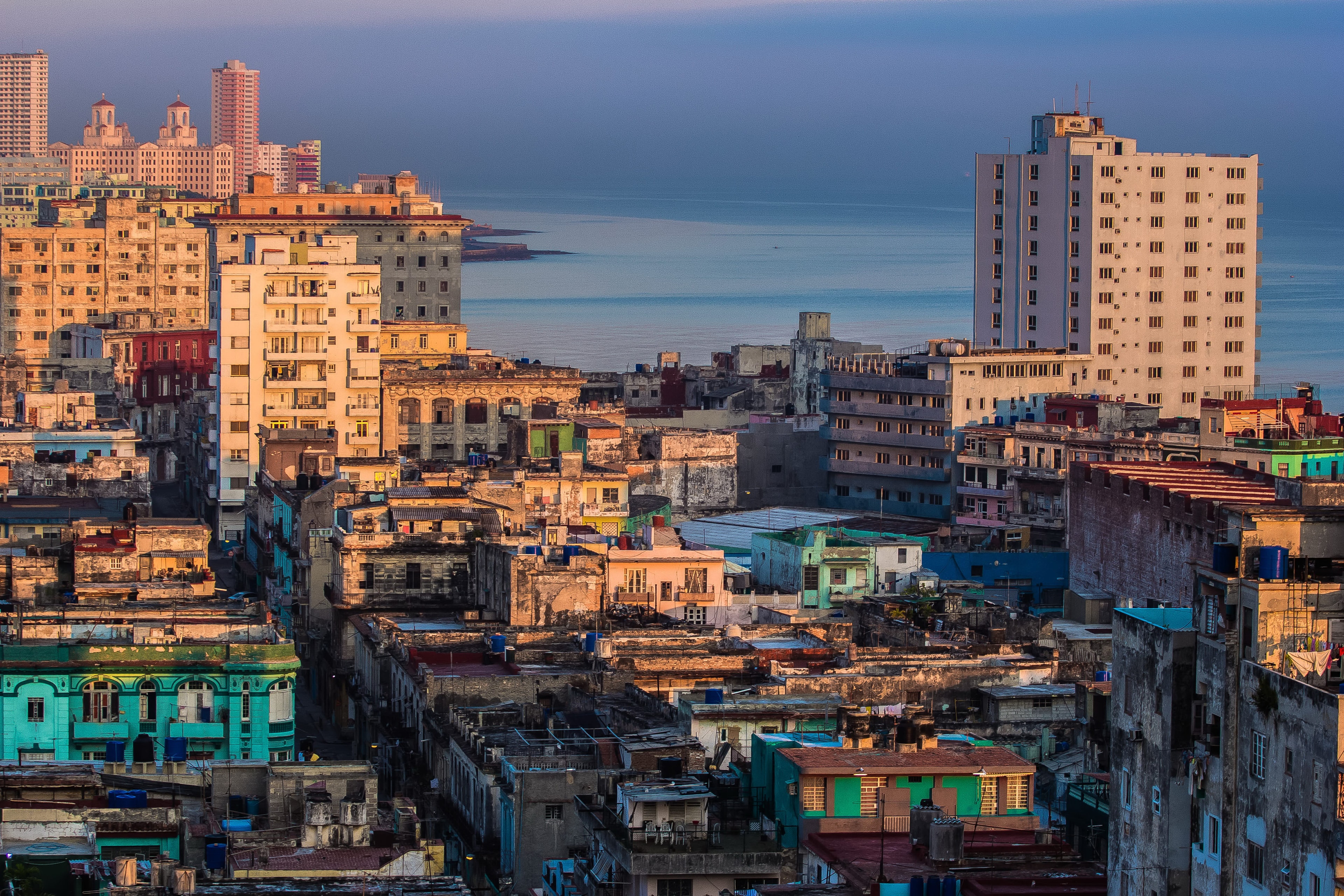 Havana rooftop panorama at dawn with colorful crumbling buildings, teal and pastel facades, and the Caribbean sea in the background, Cuba