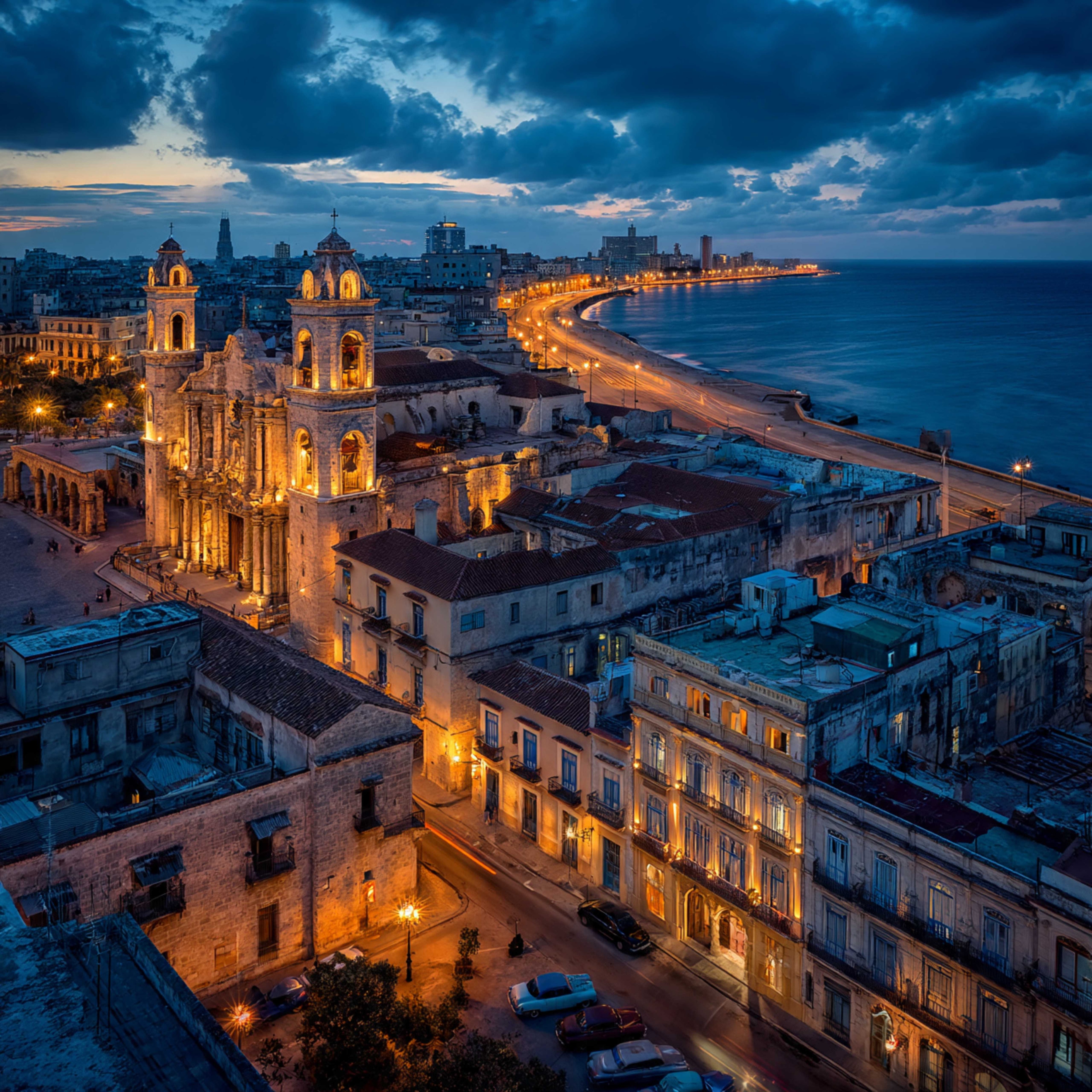Aerial blue-hour view of Old Havana with illuminated baroque cathedral towers, rooftops, vintage cars on the street below, and the Malecón curving along the sea, Cuba