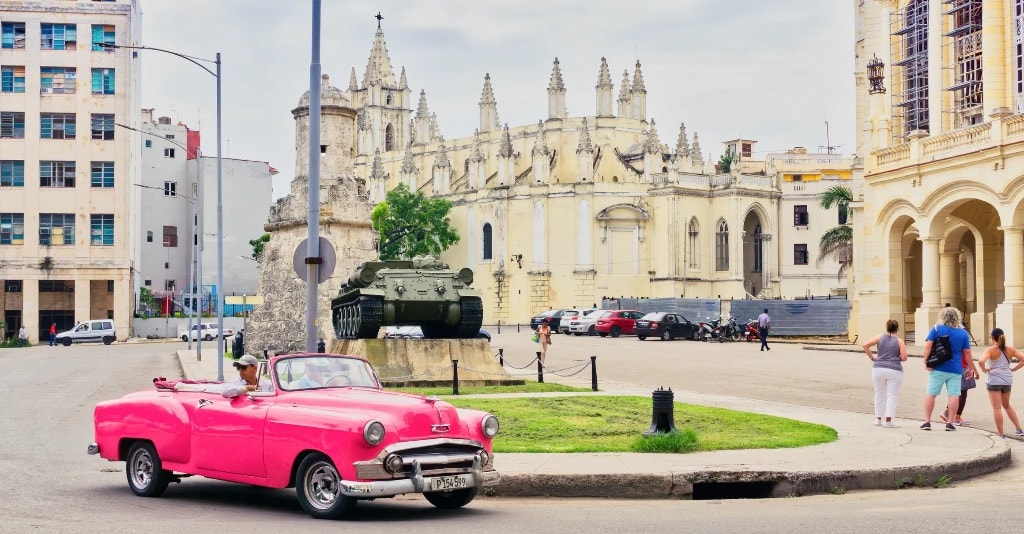 Pink vintage convertible in front of Havana church and tank monument Cuba