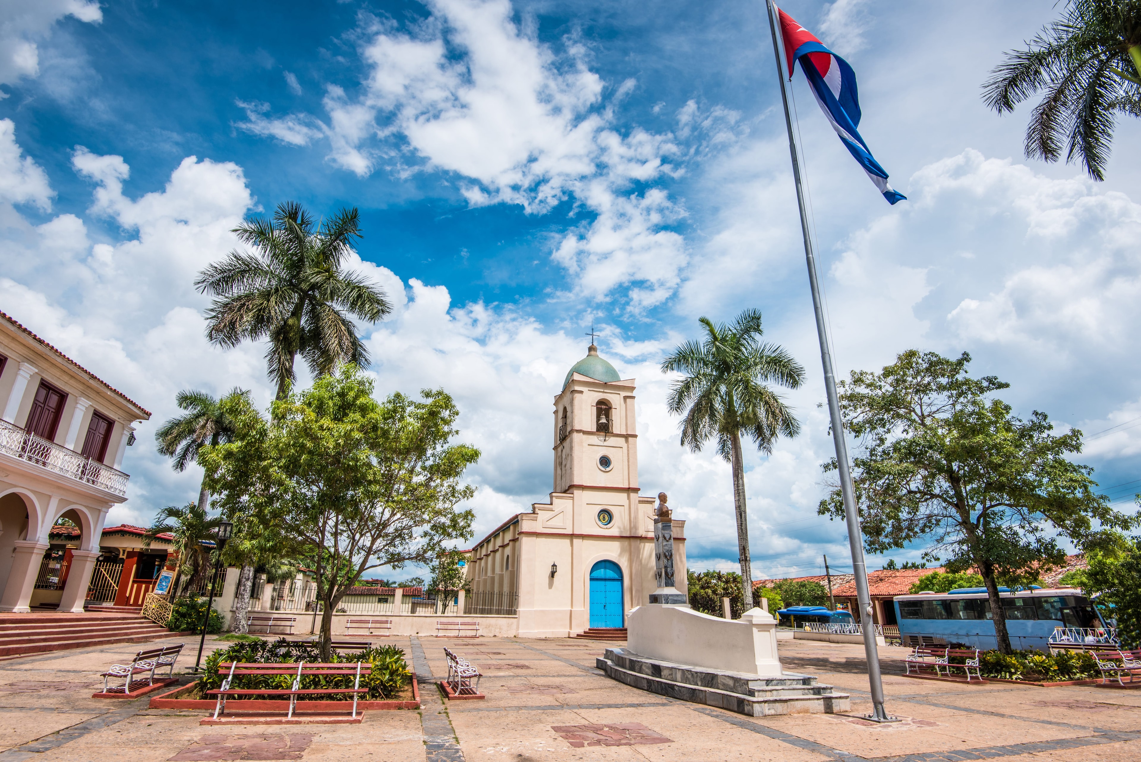 Viñales Cuba town square with colonial church, Cuban flag, and palm trees under blue sky
