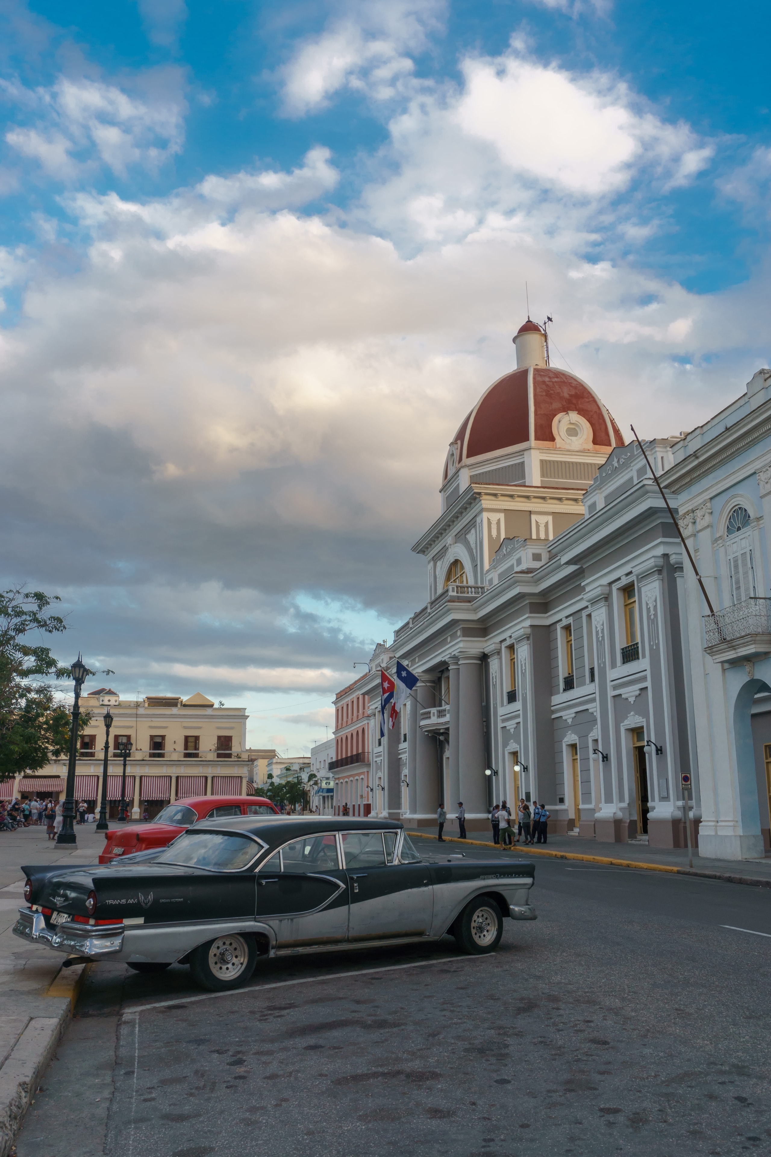 Vintage black classic car outside Cienfuegos City Hall with red dome and Cuban flag at dusk