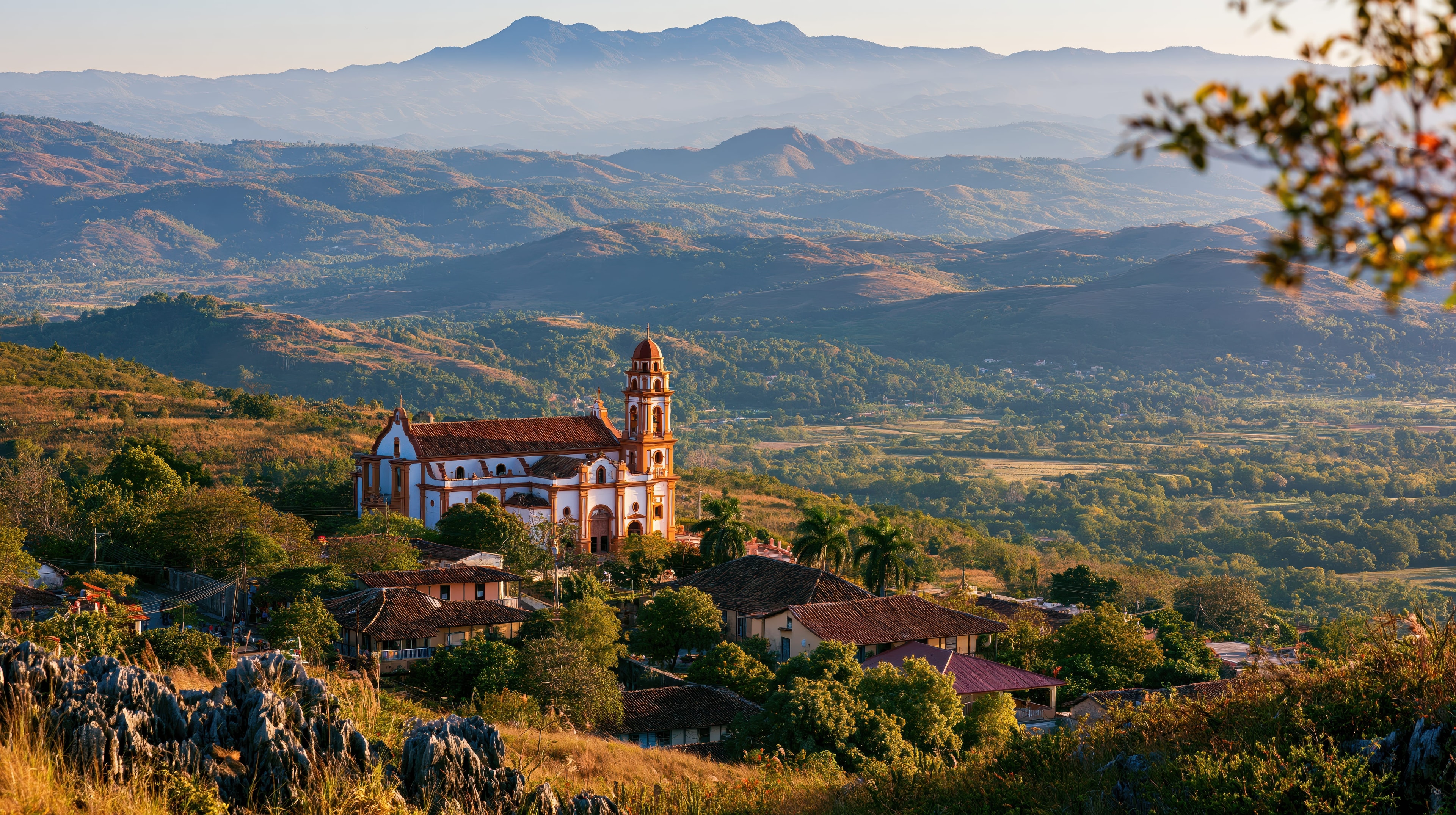 Colonial church on hilltop village surrounded by misty mountains and valley at golden hour, Cuba