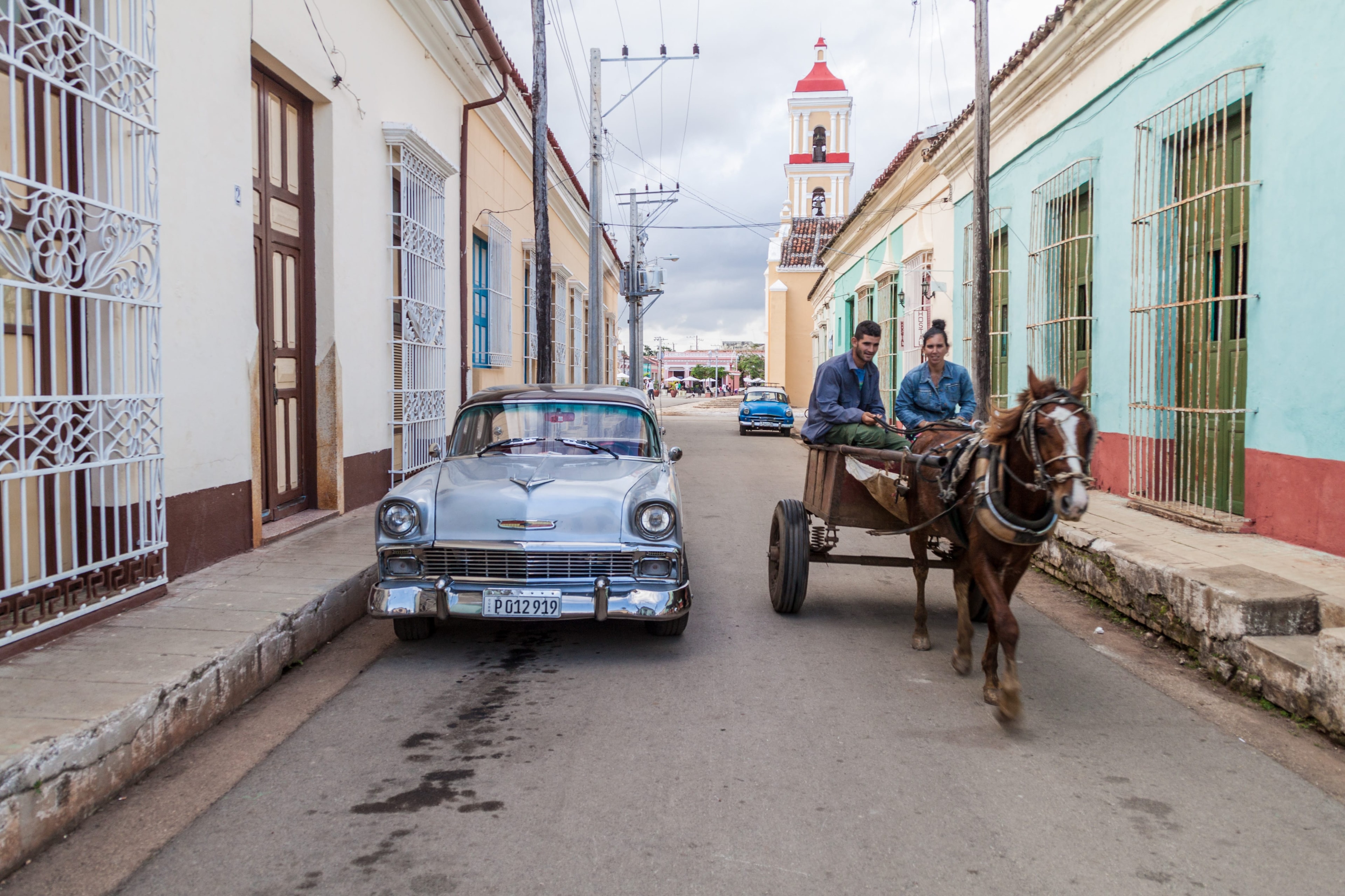 Silver vintage Chevrolet and horse-drawn cart on colonial street with church tower, Cuba