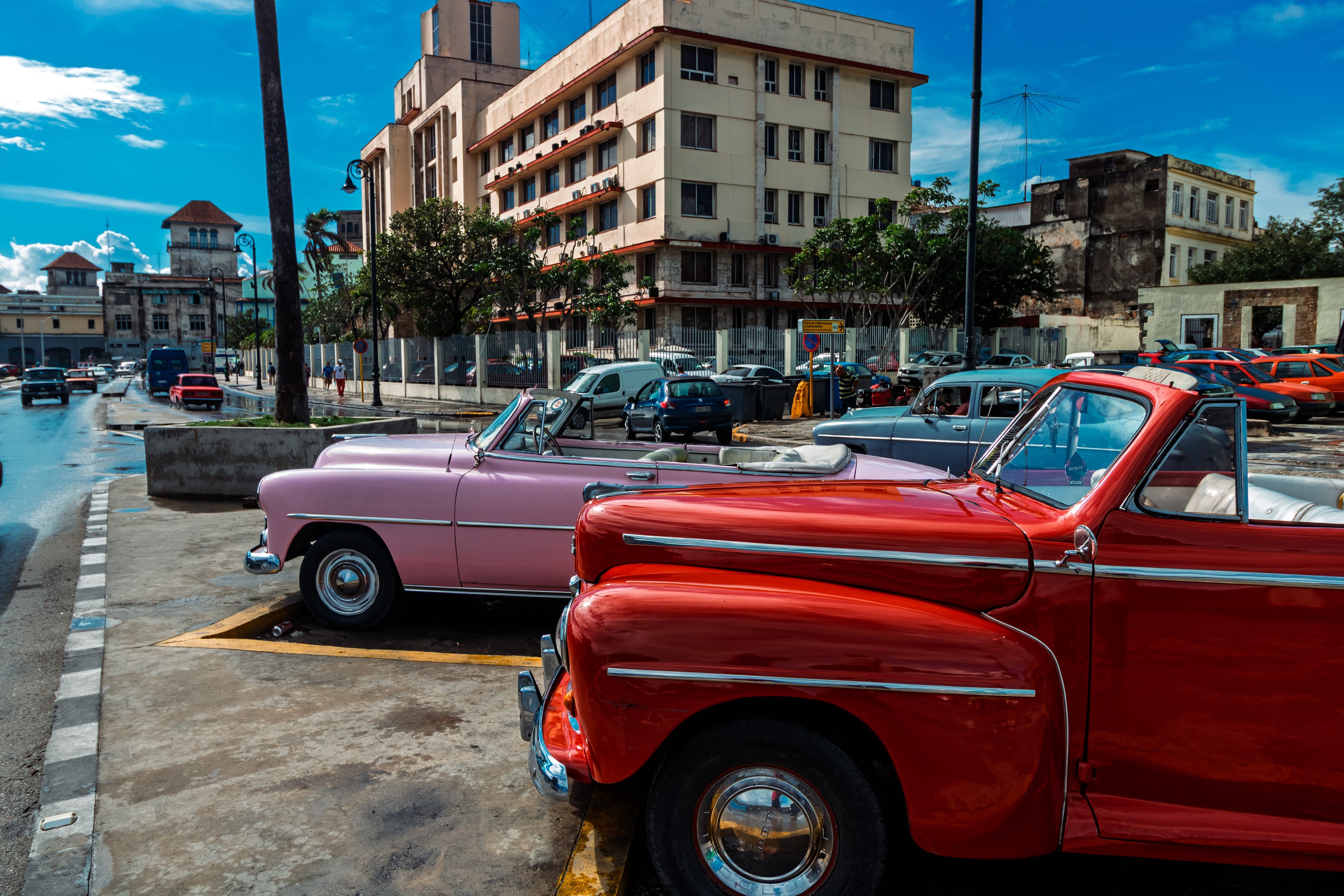 Red and pink vintage convertibles parked on Havana street under bright blue sky, Cuba