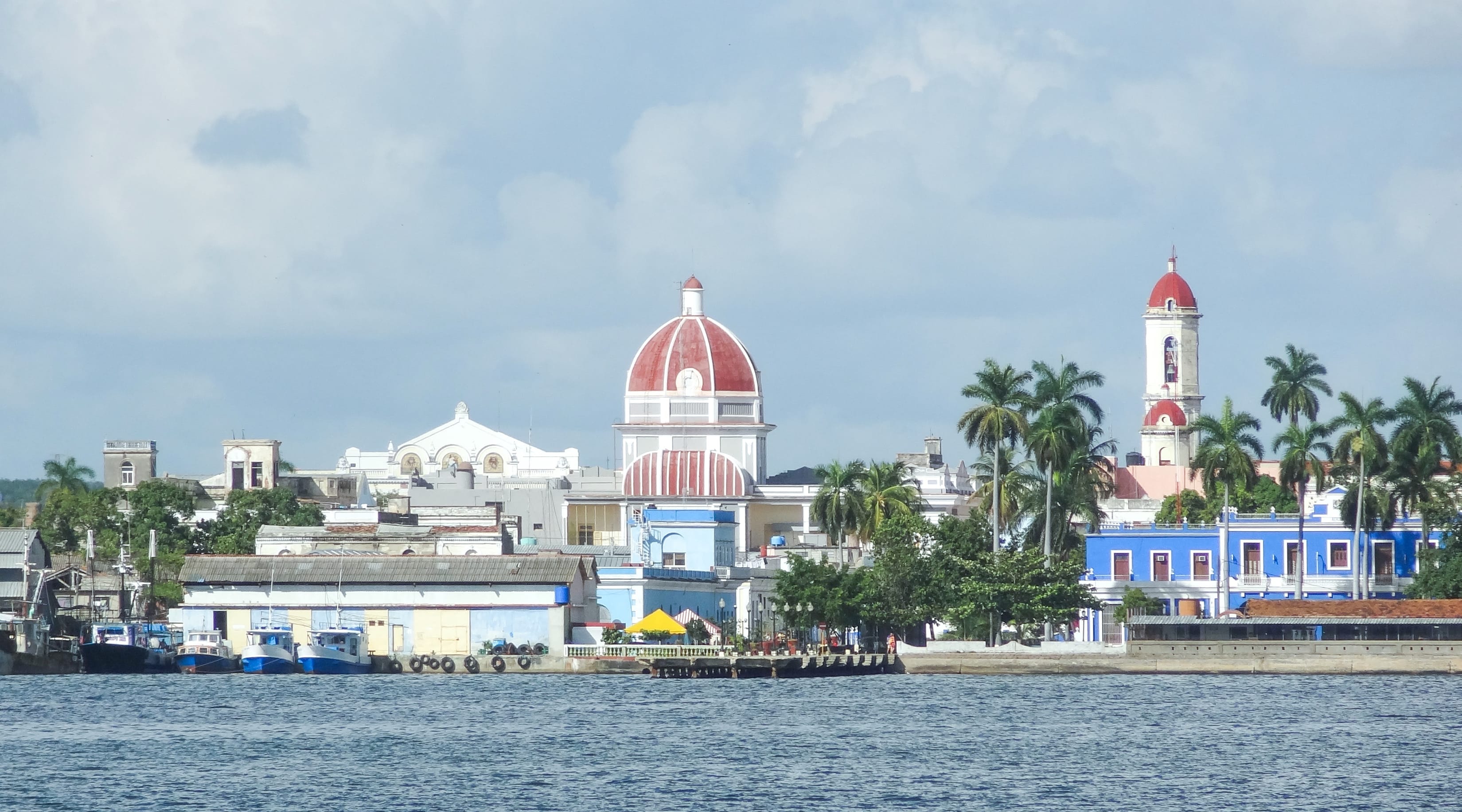 Cienfuegos colonial waterfront with red-domed buildings and palm trees seen from the harbor, Cuba